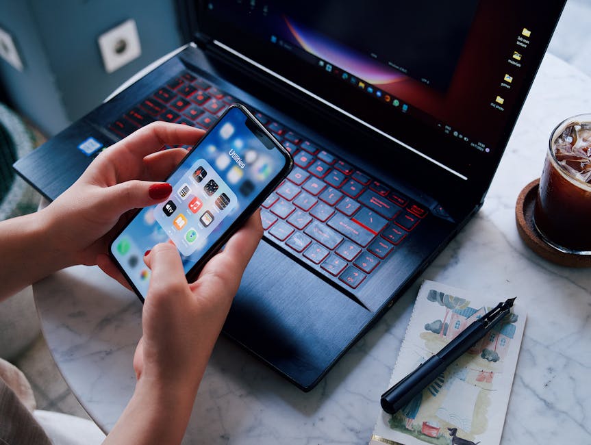 Hands holding a smartphone over a laptop with iced drink. Modern technology in everyday life.