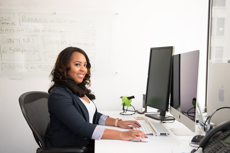 Confident businesswoman seated at her desk in an office, typing on a computer.