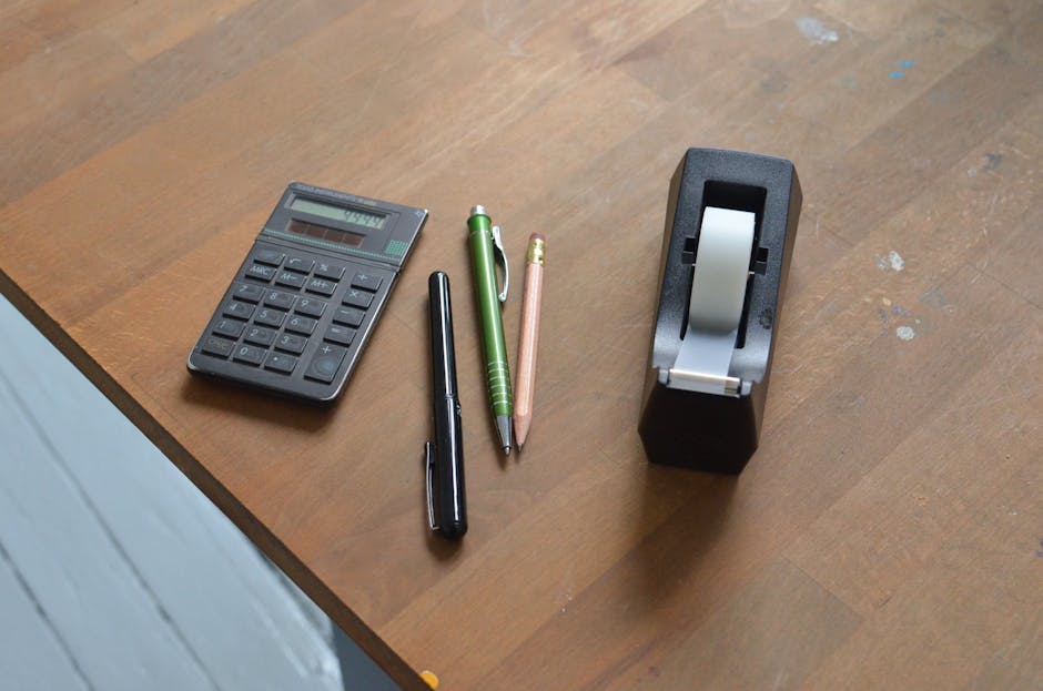 From above of small calculator pens and tape dispenser on wooden desk in office