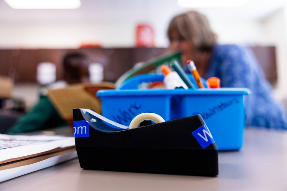 A focused shot of a tape dispenser and school supplies in a classroom environment.