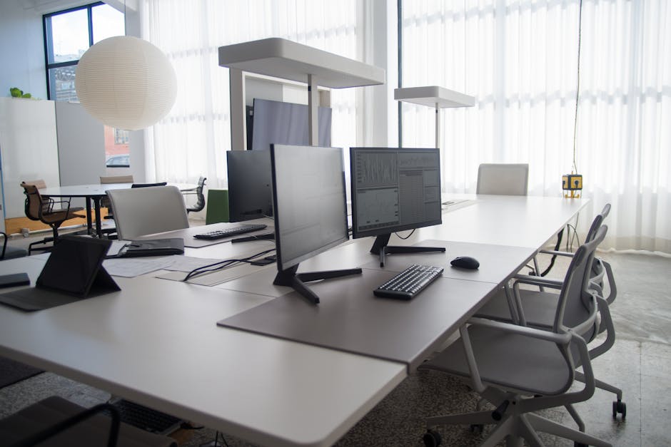 Spacious modern office featuring multiple computers, chairs, and collaborative workstations in natural light.