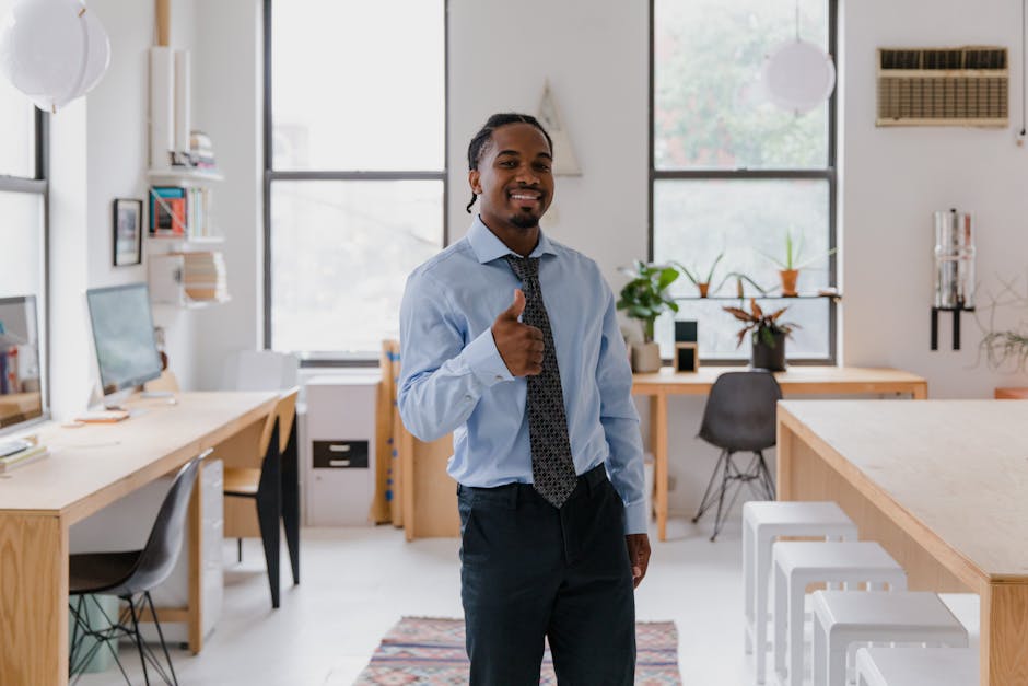 Smiling man in formalwear showing thumbs up gesture in a bright, modern office setting.